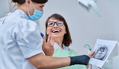 Woman smiling with dentist while reviewing X-ray