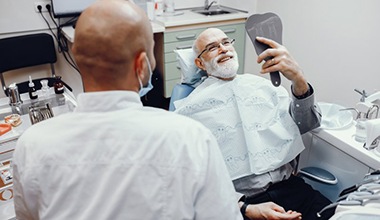 senior dental patient admiring his new smile in a mirror 