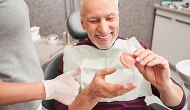 Older male looking at dentures and smiling