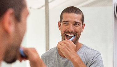 Man smiling in mirror while brushing his teeth