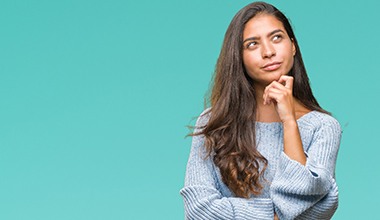 A young woman thinking, looking up, and touching her chin.