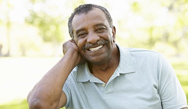 An older man with dental implants in Worthington smiling outside.
