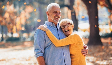 Older couple with dental implants in Worthington smiling and hugging.