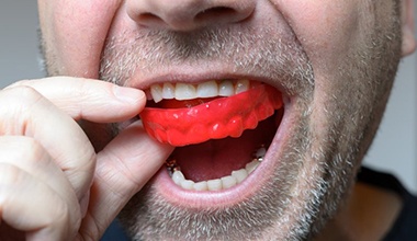 man putting a red mouthguard in his mouth 