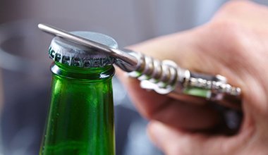 person opening a glass bottle with a bottle opener 