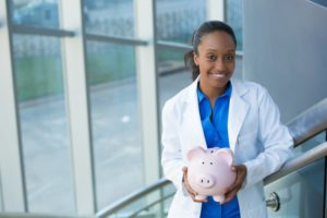 smiling dentist in Worthington holding pink piggy bank 