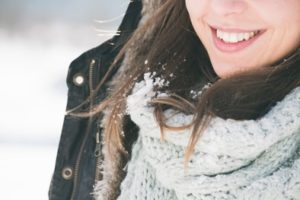 Woman with snow in her hair is wearing a coat winter scarf and smiling