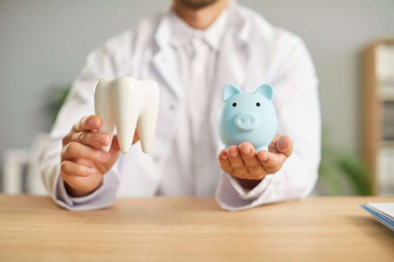 A dentist holding a large model tooth and a blue piggy bank